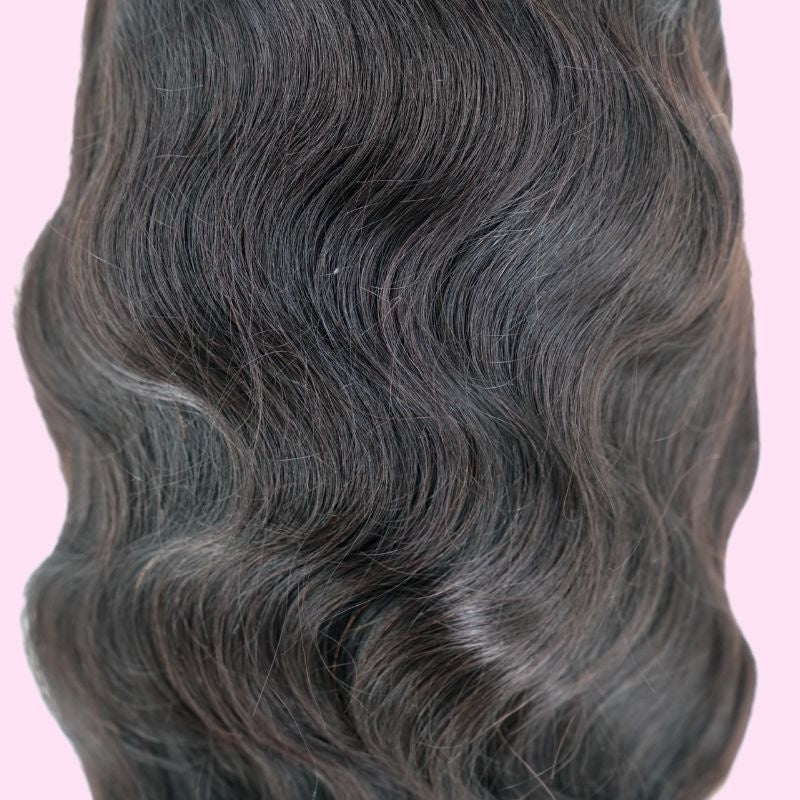 Close-up of the wave pattern on a body wave natural black human hair wig shot against a pink background