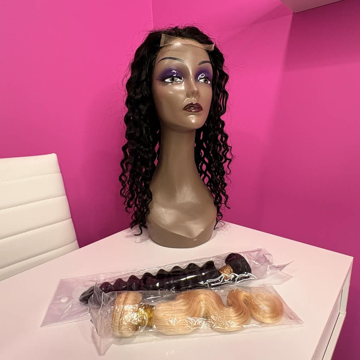 Wide showroom shot of 22 inch deep wave lace front human hair wig on mannequin with bundled hair extensions on table