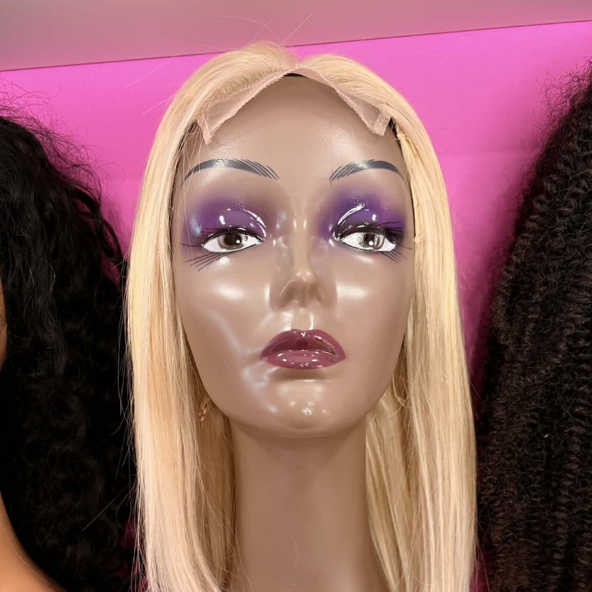 Front view of 10 inch blonde bob human hair wig on mannequin between other wigs in showroom showing straight chin-length styling