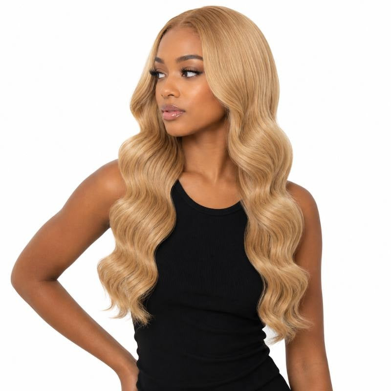 Model wearing honey blonde 27 body wave sew-in hair extensions installed with a middle part and long waves on a white background