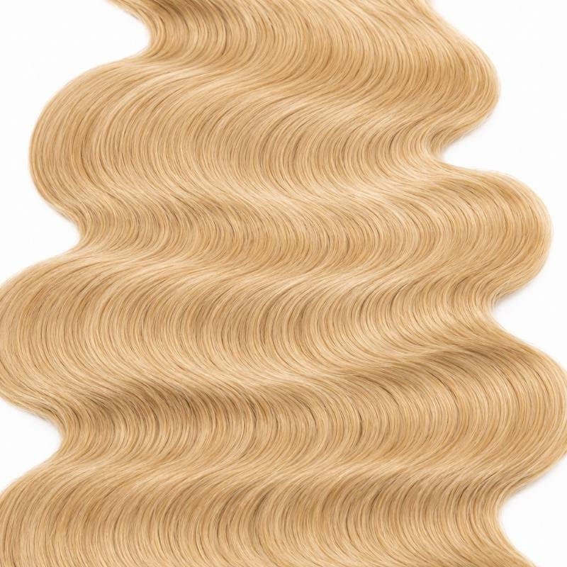 Macro crop of the S shaped wave pattern in honey blonde 27 body wave sew-in hair extensions filling the frame on white