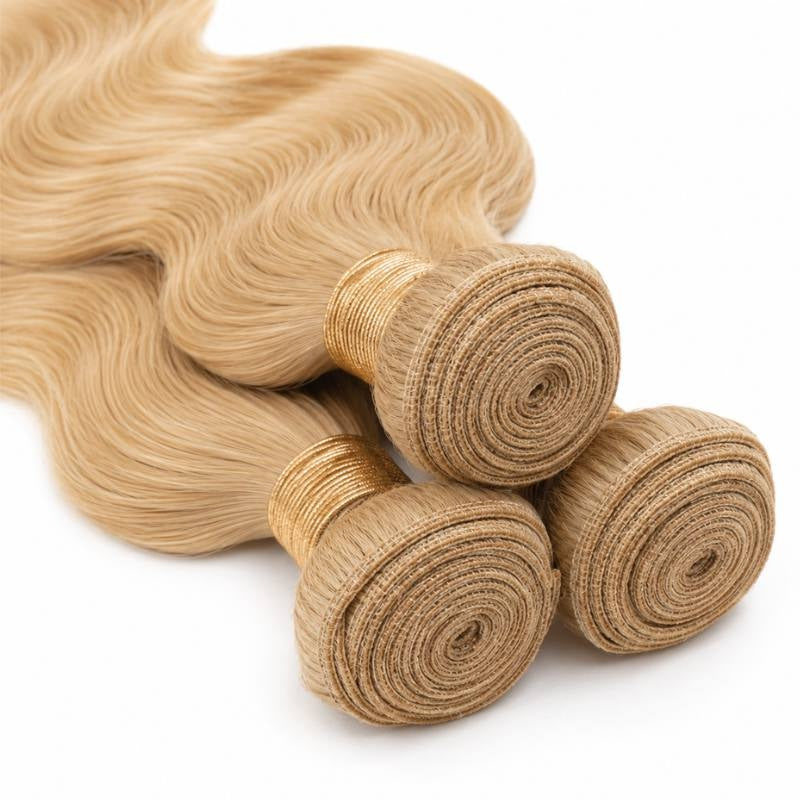 Close-up of the coiled wefts and gold bands on three bundles of honey blonde 27 body wave sew-in hair extensions laid on white