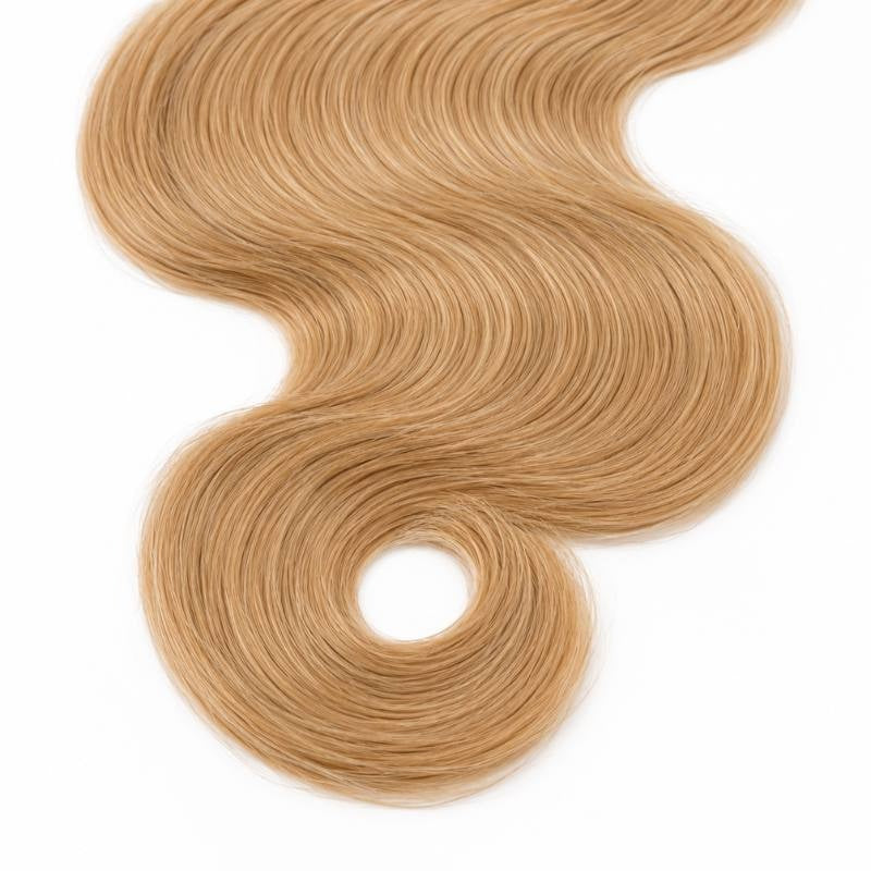 Close view of the curled end on a single bundle of honey blonde 27 body wave sew-in hair extensions laid on a white surface