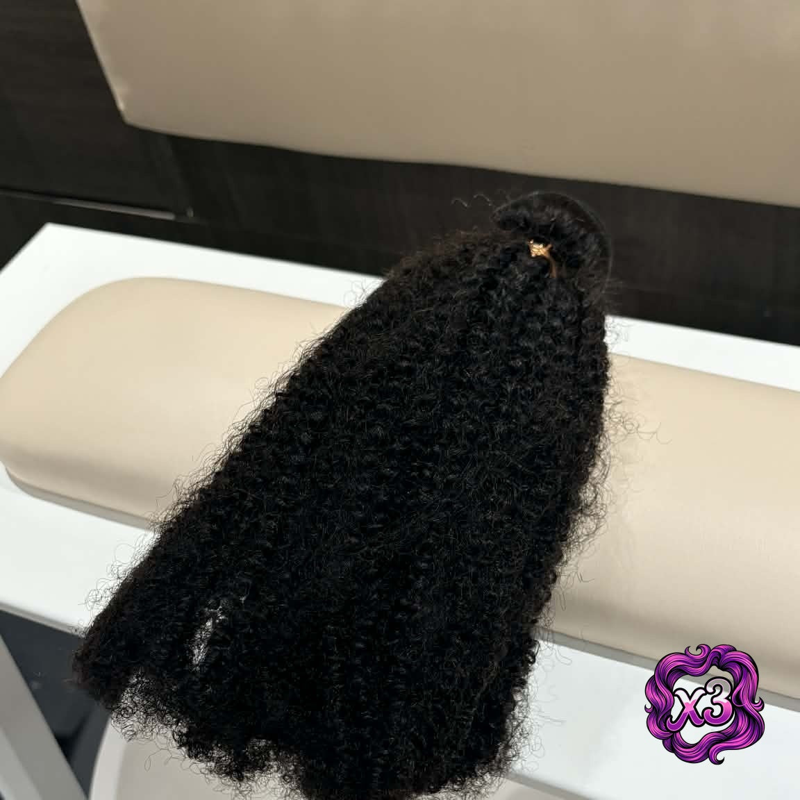 3 bundle deal — 16 inch Brazilian afro kinky curly sew-in hair extensions bundle draped over salon chair arm showing natural coil movement and volume