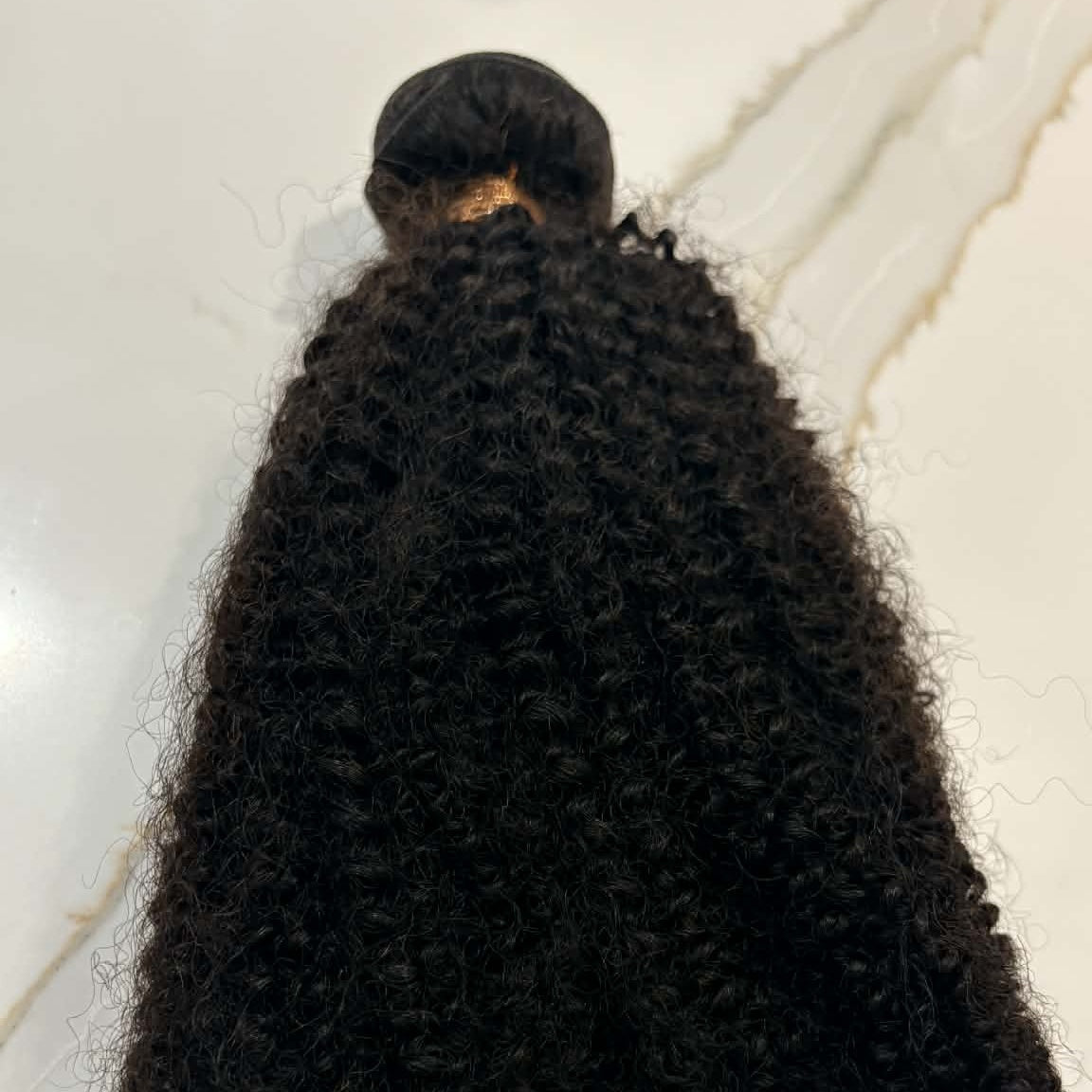 16 inch Brazilian afro kinky curly sew-in hair extensions bundle on marble surface showing dense tight coils and weft construction