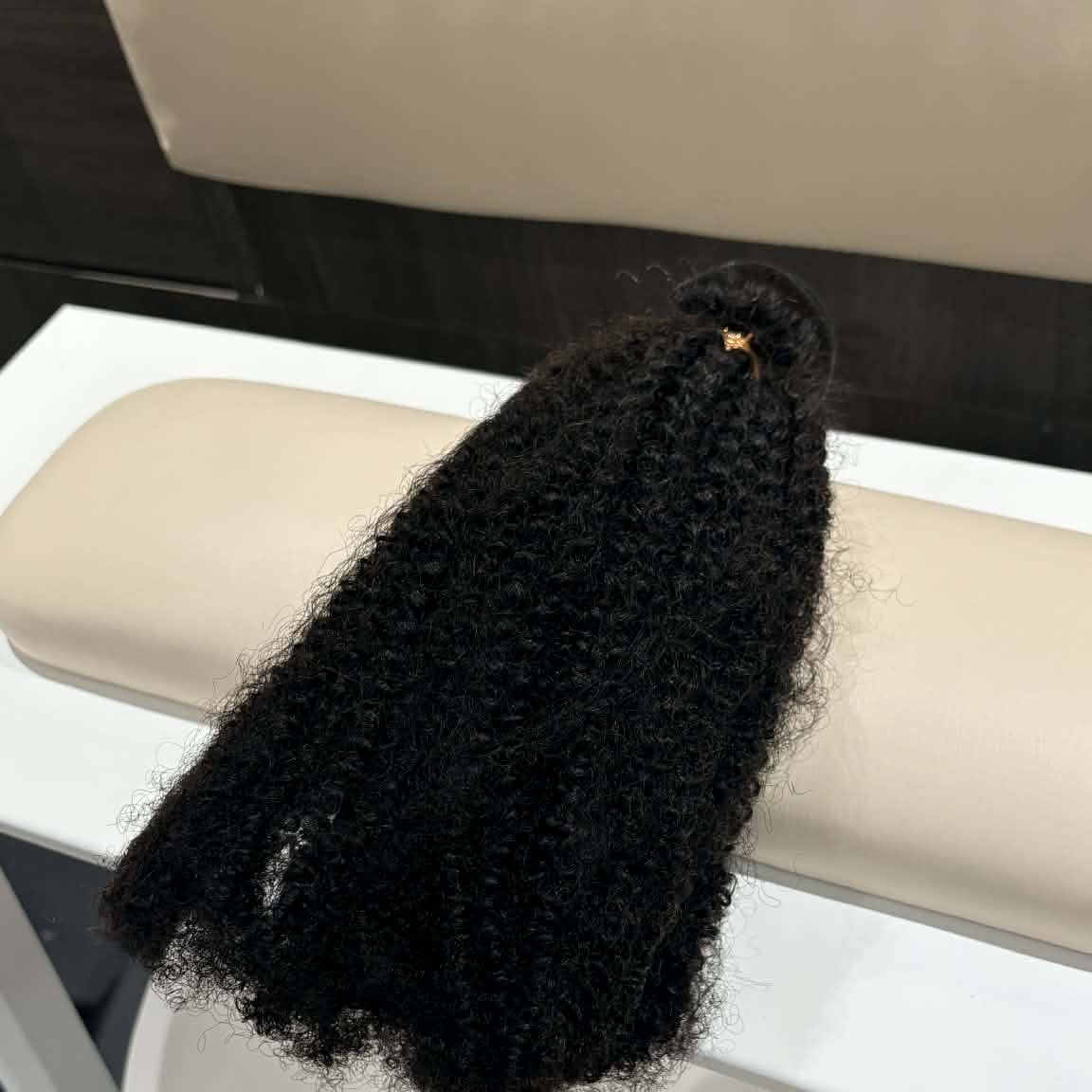 16 inch Brazilian afro kinky curly sew-in hair extensions bundle draped over salon chair arm showing natural coil movement and volume