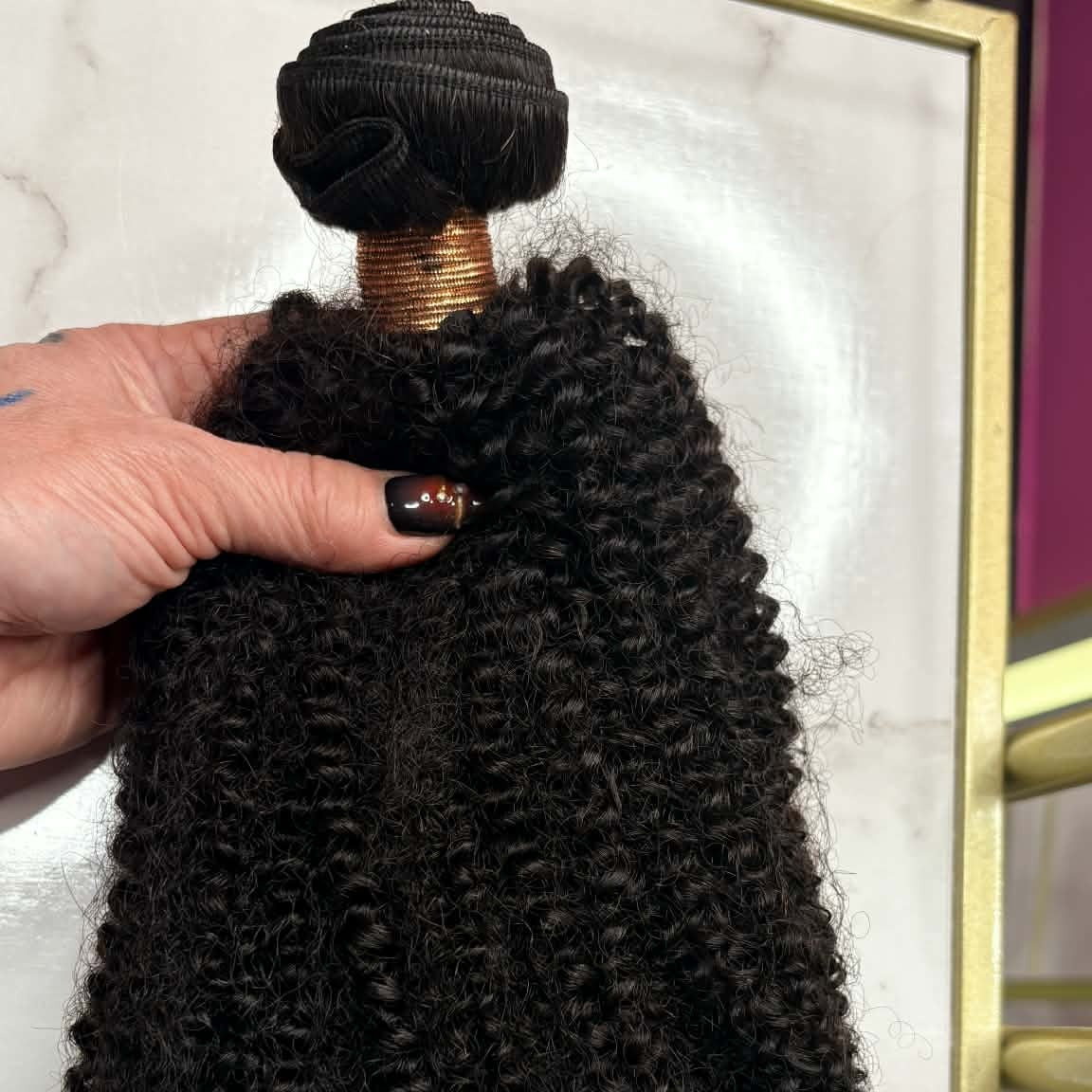 Hand holding 16 inch Brazilian afro kinky curly sew-in hair extensions bundle in gold frame showing dense coil texture and volume