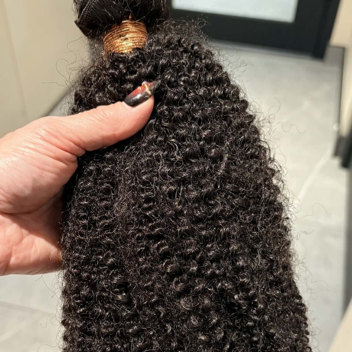 Hand holding 16 inch Brazilian afro kinky curly sew-in hair extensions bundle showing weft track at top and dense coil pattern