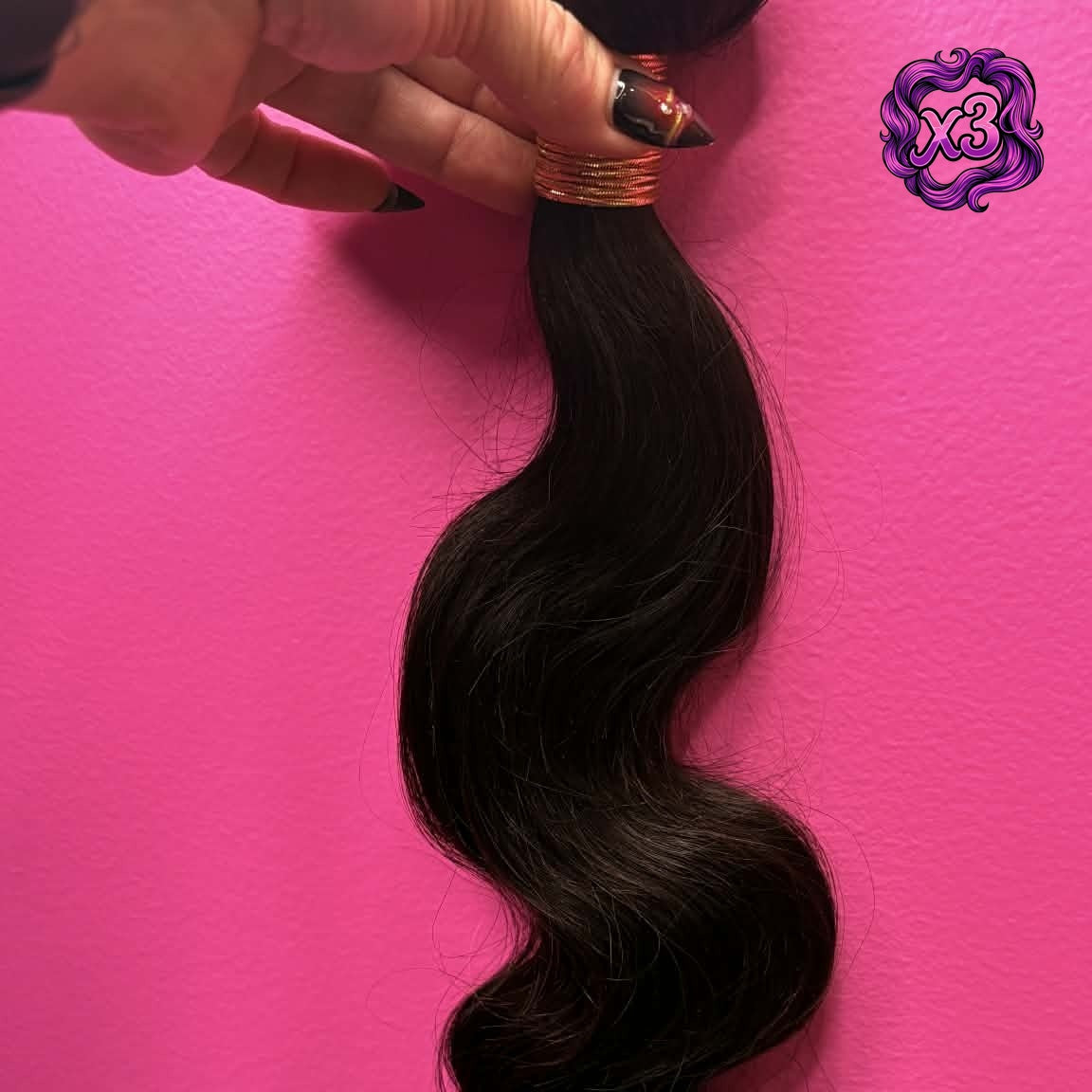 3 bundle deal — Hand holding 16 inch Brazilian body wave sew-in hair extensions bundle against pink wall showing weft track and flowing S-wave texture