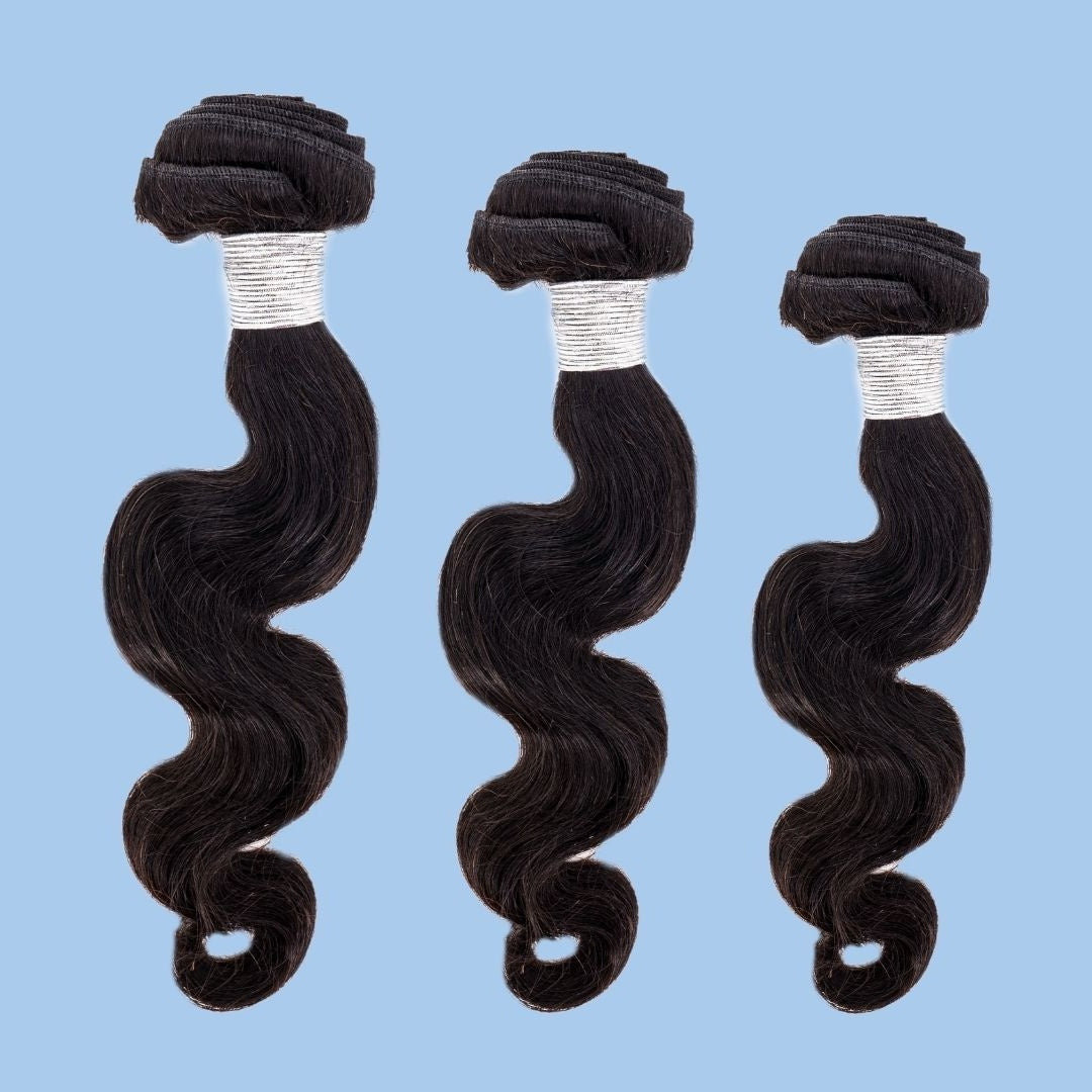 Three bundles of natural black body wave sew-in hair extensions in graduated lengths on a blue backdrop with white thread wrapping the wefts
