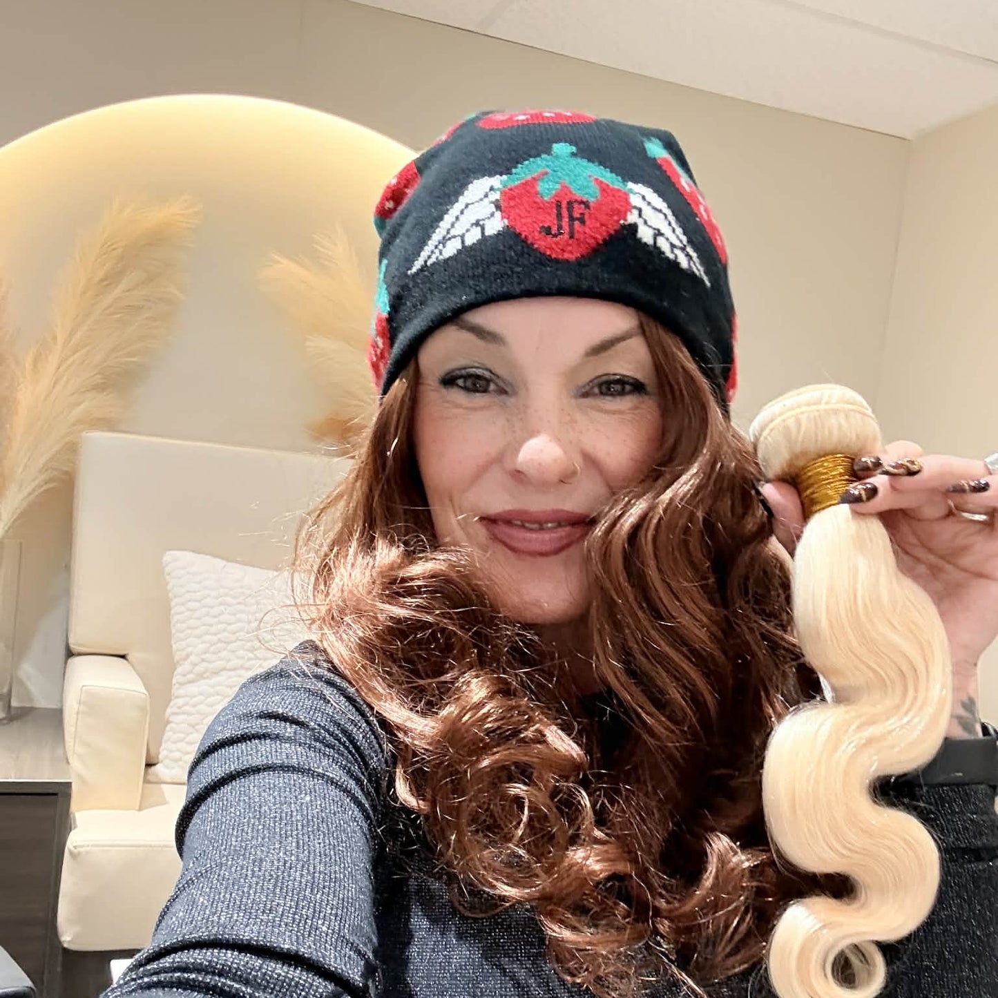Salon owner holding 16 inch blonde 613 body wave sew-in hair extensions bundle showing S-wave pattern and platinum color