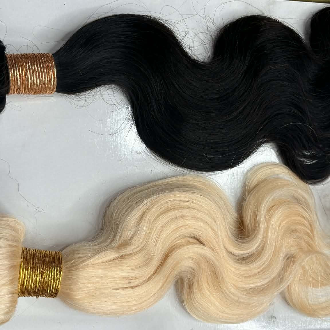 Two body wave sew-in hair extensions bundles flat lay in natural black and blonde showing weft construction and loose wave pattern