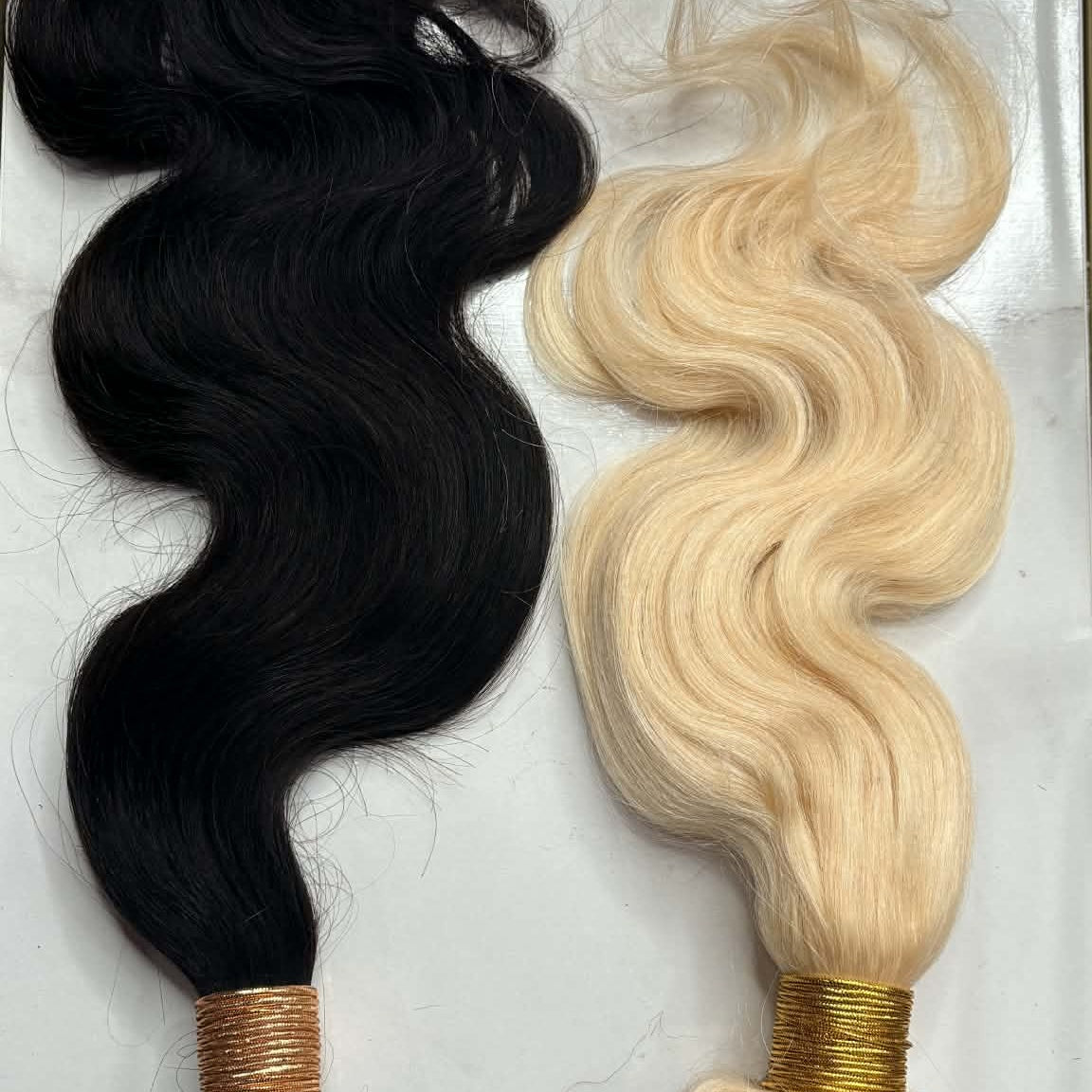 Two sew-in hair extensions bundles side by side in natural black and blonde body wave on marble showing S-wave texture comparison