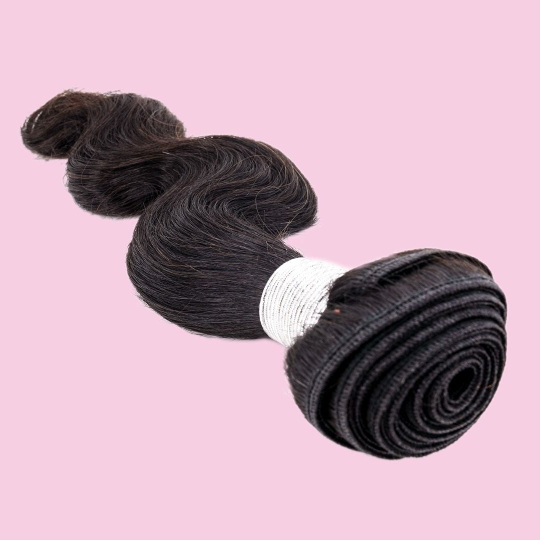 Natural black body wave sew-in hair extensions on a pink backdrop with the spiral rolled weft facing the camera and white thread wrap