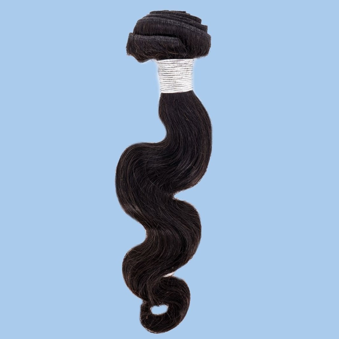 Natural black body wave sew-in hair extensions hanging on a blue backdrop with a wide white thread wrap under the folded weft
