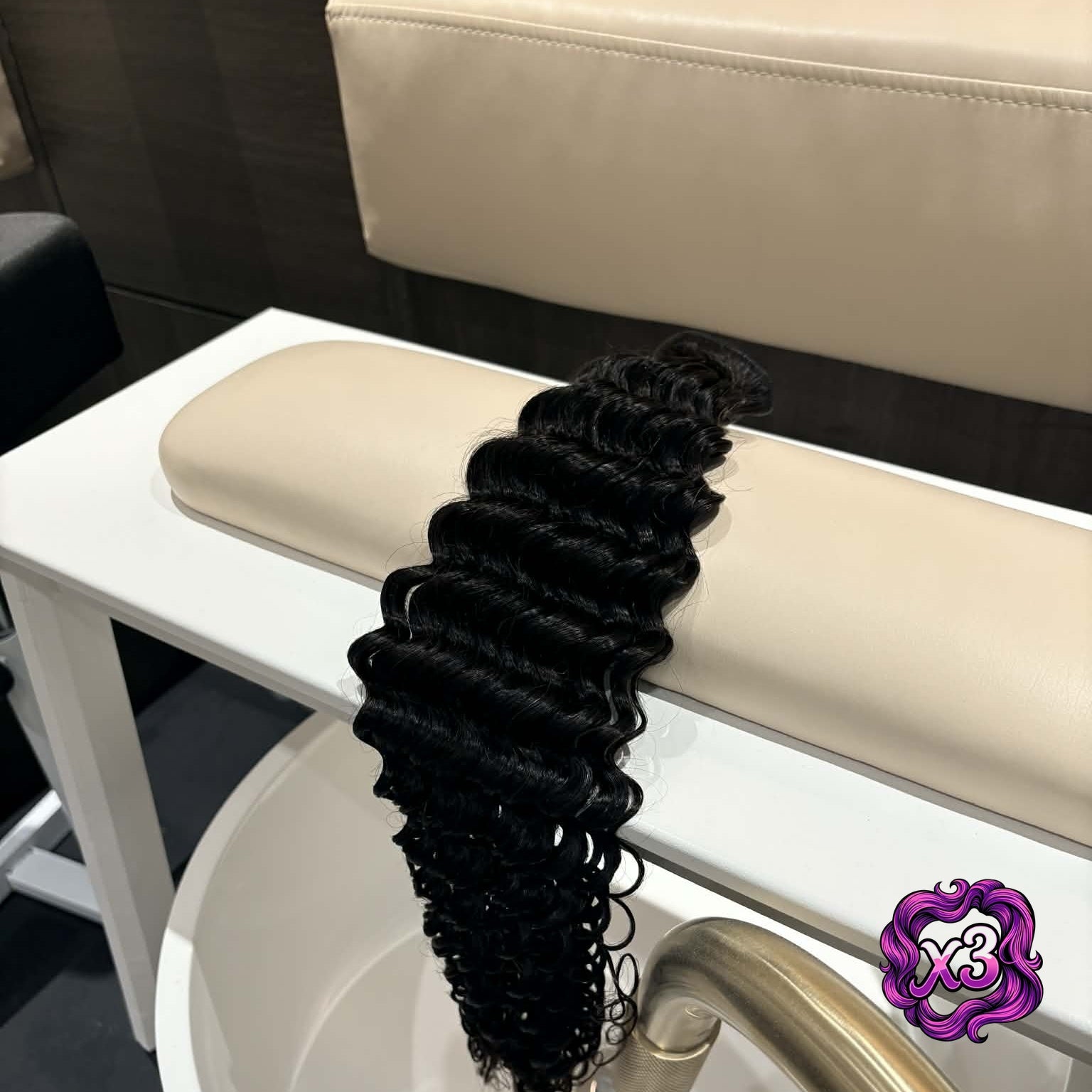3 bundle deal — 16 inch Brazilian deep wave sew-in hair extensions bundle on salon chair arm showing defined S-spiral curls hanging from weft