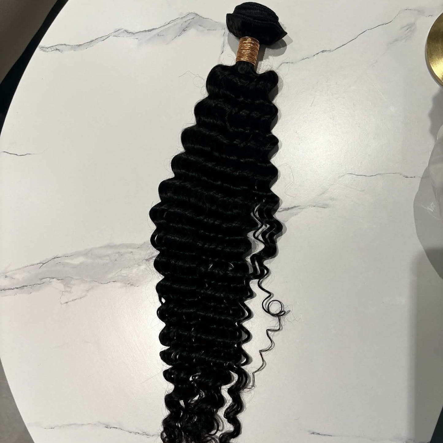 16 inch Brazilian deep wave sew-in hair extensions bundle on marble table showing full length from rubber-banded weft to curl tips