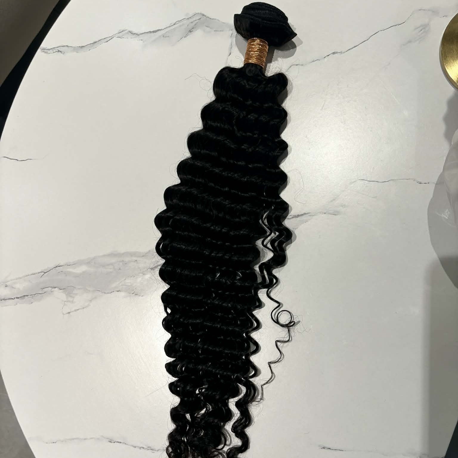 16 inch Brazilian deep wave sew-in hair extensions bundle on marble table showing full length from rubber-banded weft to curl tips