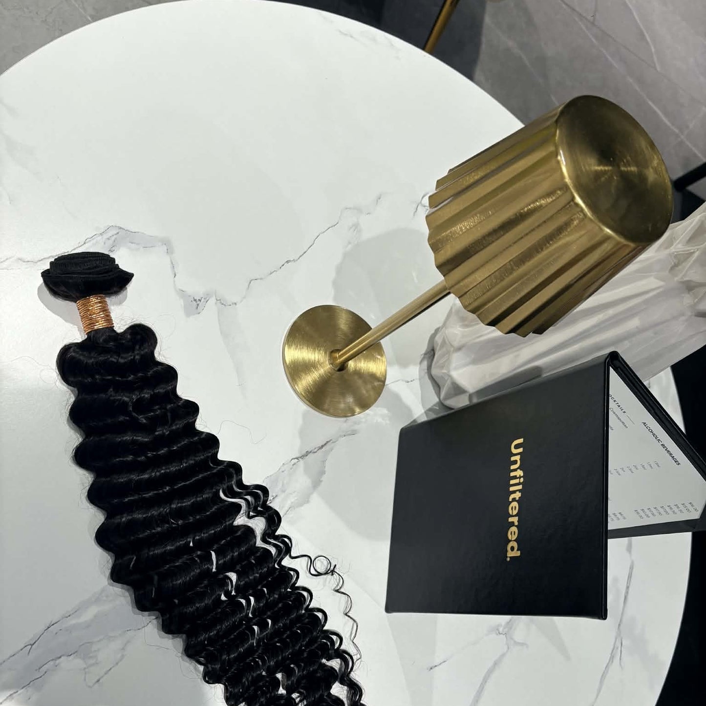 16 inch Brazilian deep wave sew-in hair extensions bundle on marble table with gold lamp and brand card showing weft and spiral curls