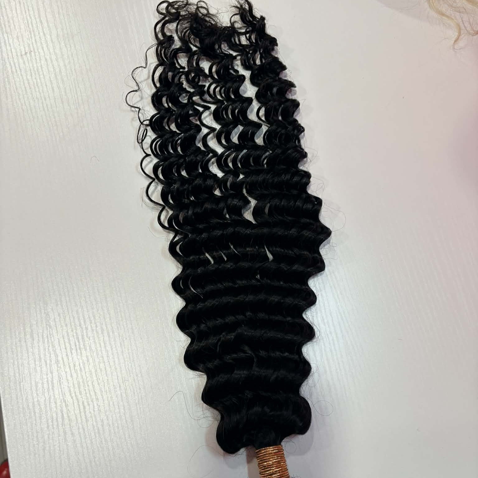 16 inch Brazilian deep wave sew-in hair extensions bundle on white surface showing rubber-banded weft and spiral curl pattern