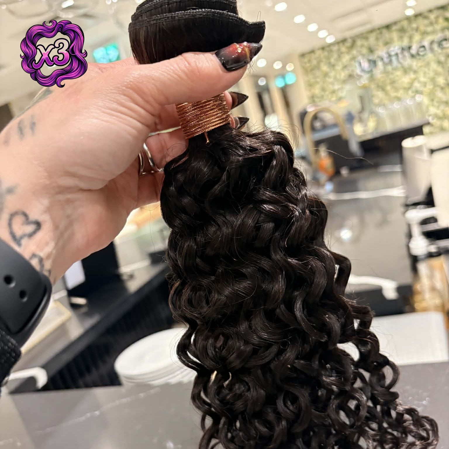 3 bundle deal — Hand holding 16 inch Brazilian kinky curly sew-in hair extensions bundle in salon showing full curl length and volume from weft to tips