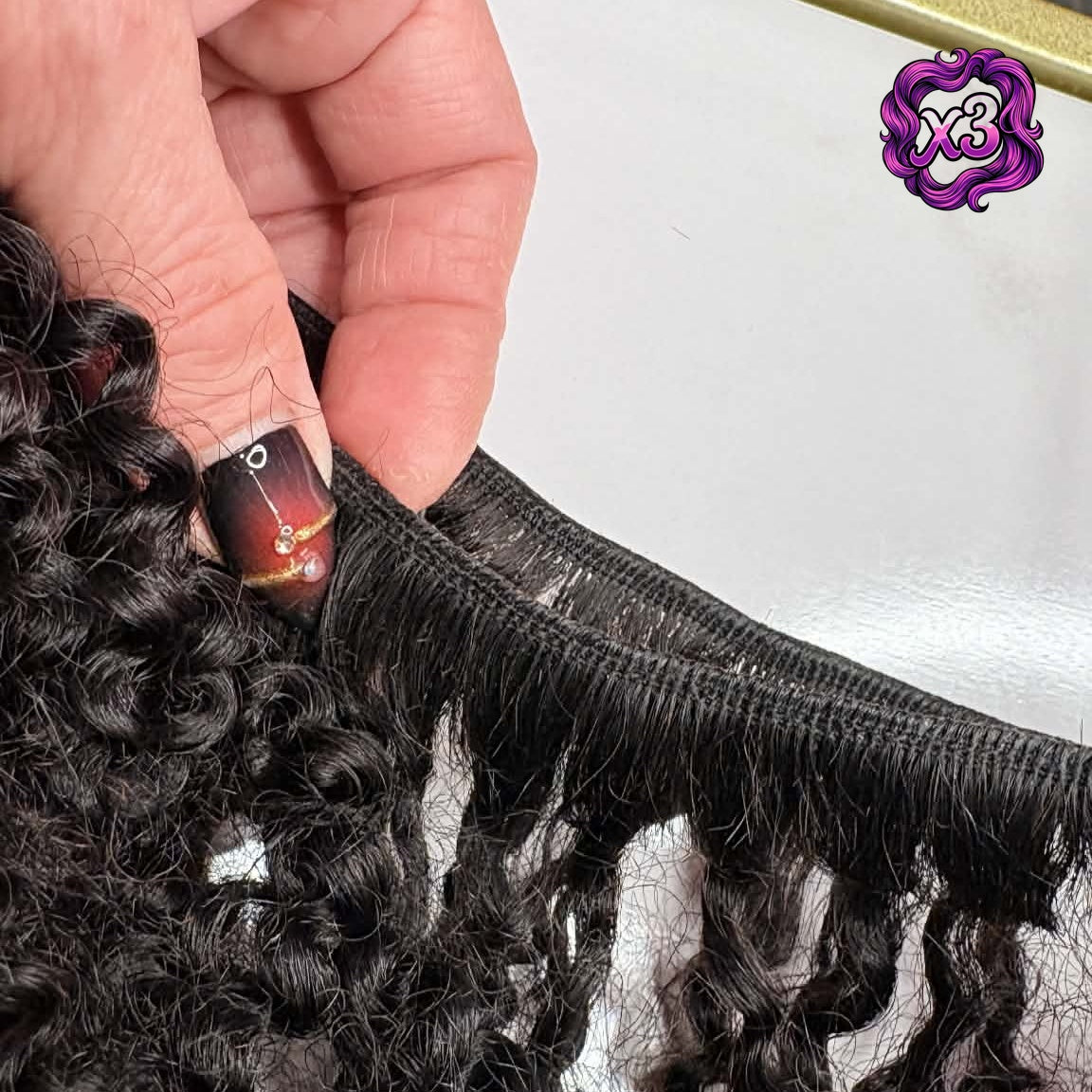 3 bundle deal — Hand holding 16 inch Brazilian kinky curly sew-in hair extensions bundle showing weft closeup with rolled weft and tight defined curls