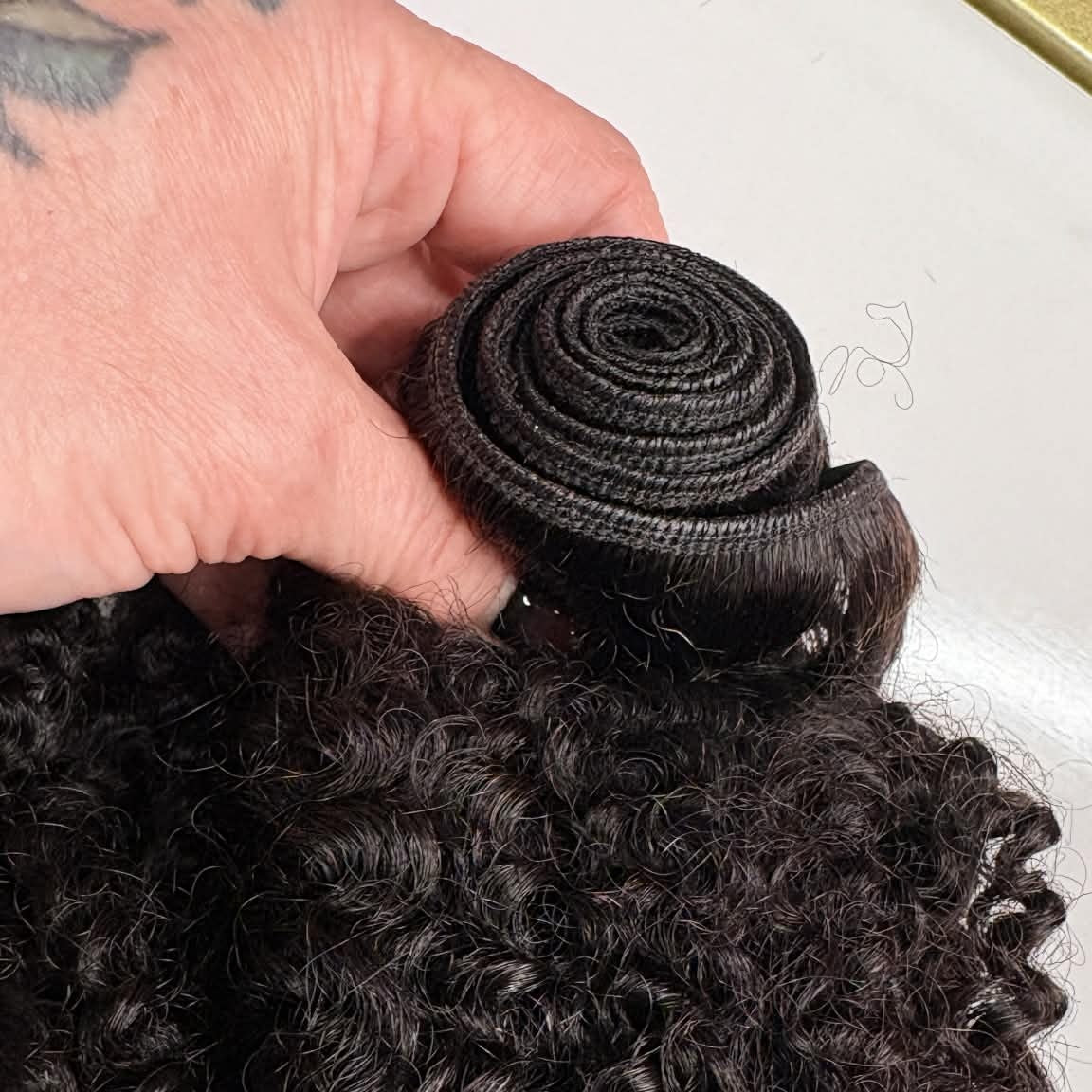 Close-up of 16 inch Brazilian kinky curly sew-in hair extensions weft showing rolled machine-made weft stitching and curl texture