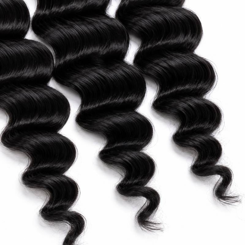 Close-up of the fanned tips of three bundles of natural black loose wave sew-in hair extensions on a white background