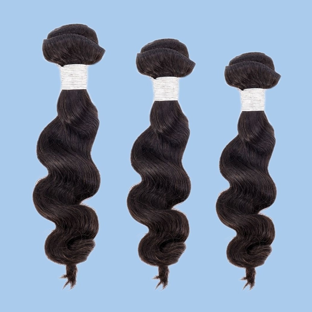 Three bundles of natural black loose wave sew-in hair extensions in descending sizes on a blue backdrop with white thread wrapped around each weft