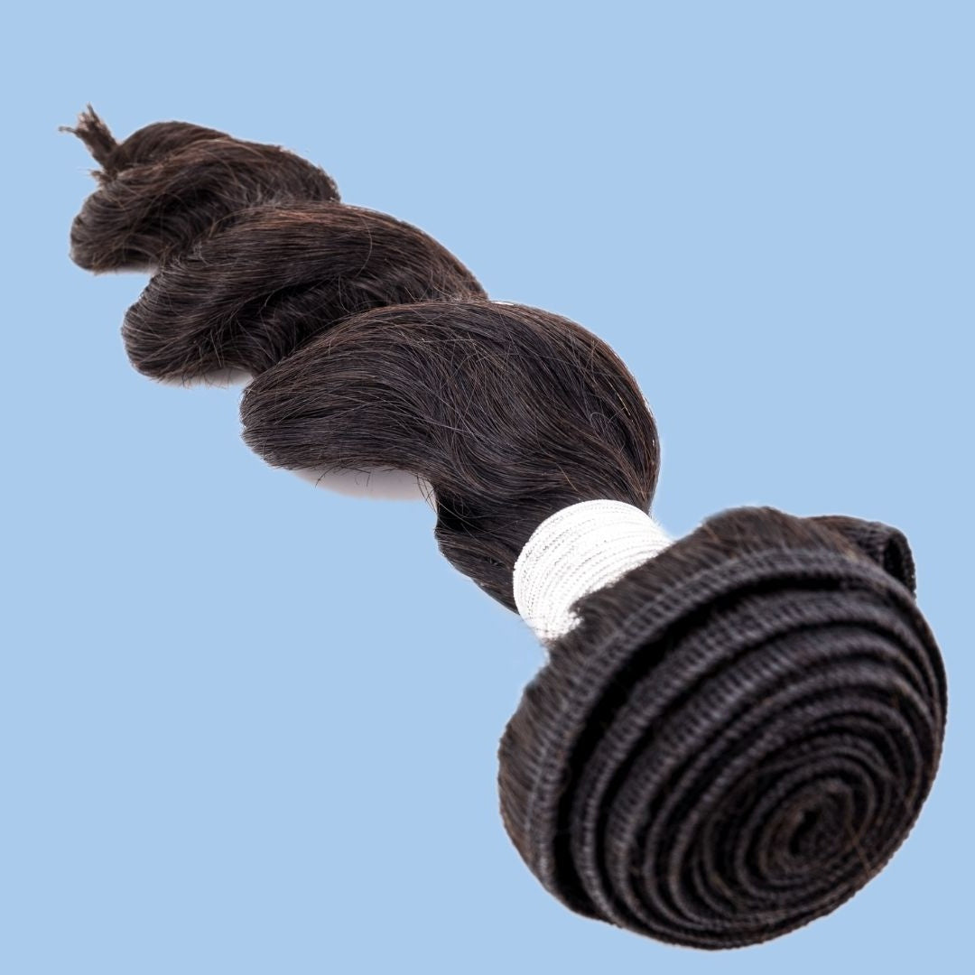 Natural black loose wave sew-in hair extensions laid diagonally on a blue backdrop with a white thread wrap and the coiled weft in the foreground