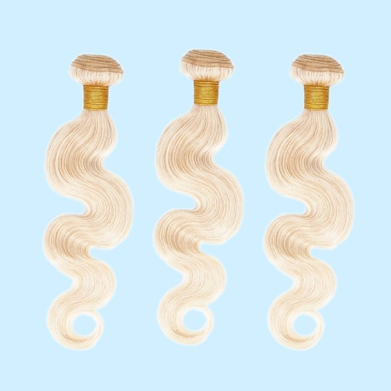 Three bundles of blonde body wave sew-in hair extensions on a pale blue backdrop with the wave pattern curling at the ends