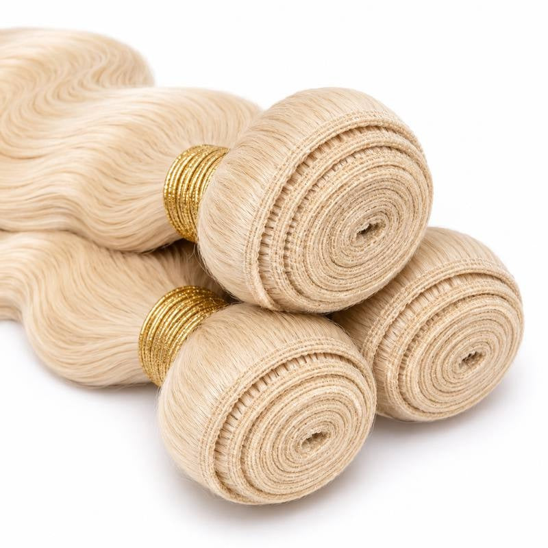 Close-up of the coiled wefts on three bundles of blonde body wave sew-in hair extensions bound with gold thread