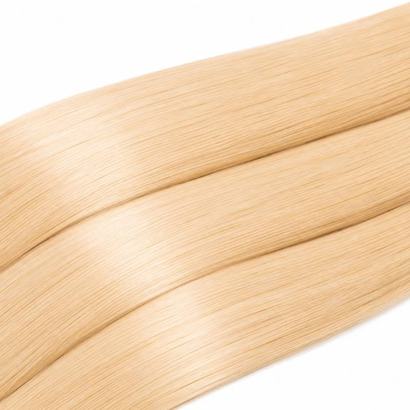 Macro view of three lengths of blonde straight sew-in hair extensions laid diagonally showing smooth strands and reflected light