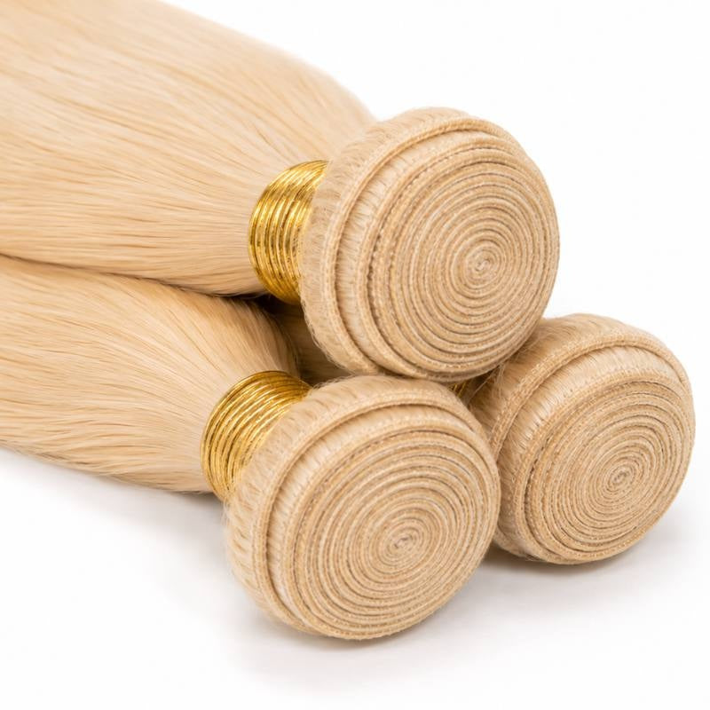 Close-up of the coiled wefts on three bundles of blonde straight sew-in hair extensions bound with gold thread