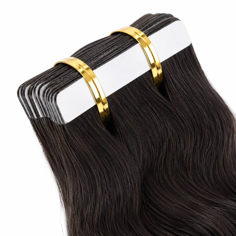 Close-up of the white adhesive tape tabs at the top of natural black body wave tape-in hair extensions held in a banded stack