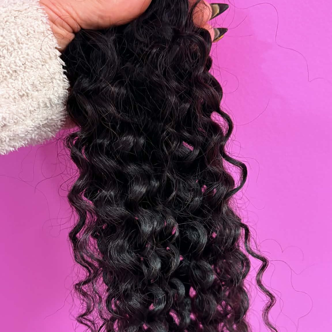 Hand holding 16 inch kinky curly 3B-3C tape-in hair extensions against pink wall showing tape tabs and full curl length