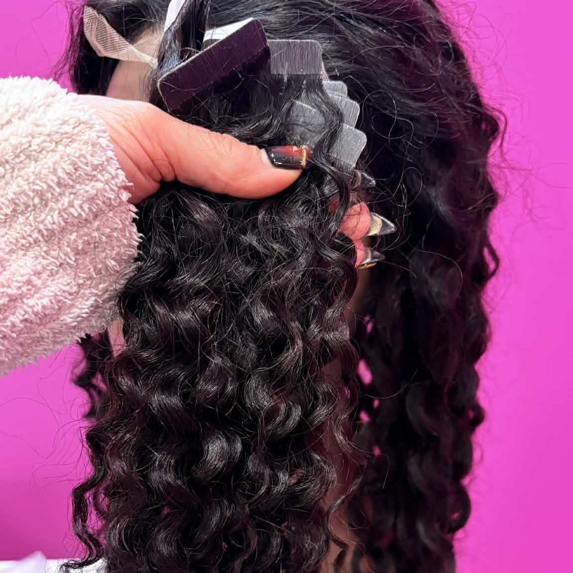 Hand holding 16 inch kinky curly 3B-3C tape-in hair extensions showing tape tabs at top and curly hair hanging down